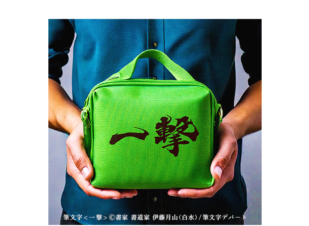 マチ付きの緑色のポーチ（小物入れ）の表面に堂々と大きく印字された「一撃」の毛筆書体が印象的です。この筆文字は月山書体 風の舞フォントを採用しています。このポーチを若い男性が両手で持った画像です。